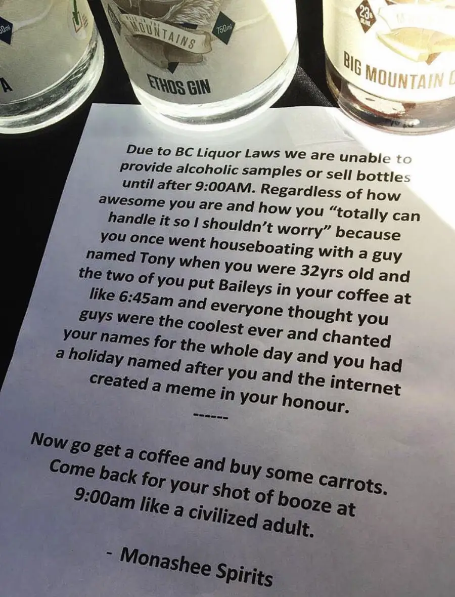A sign from Monashee Spirits explains BC liquor law restrictions before 9:00 AM, humorously recalling a houseboating trip, and suggests getting coffee and carrots until it’s legal to buy alcohol at 9:00 AM.