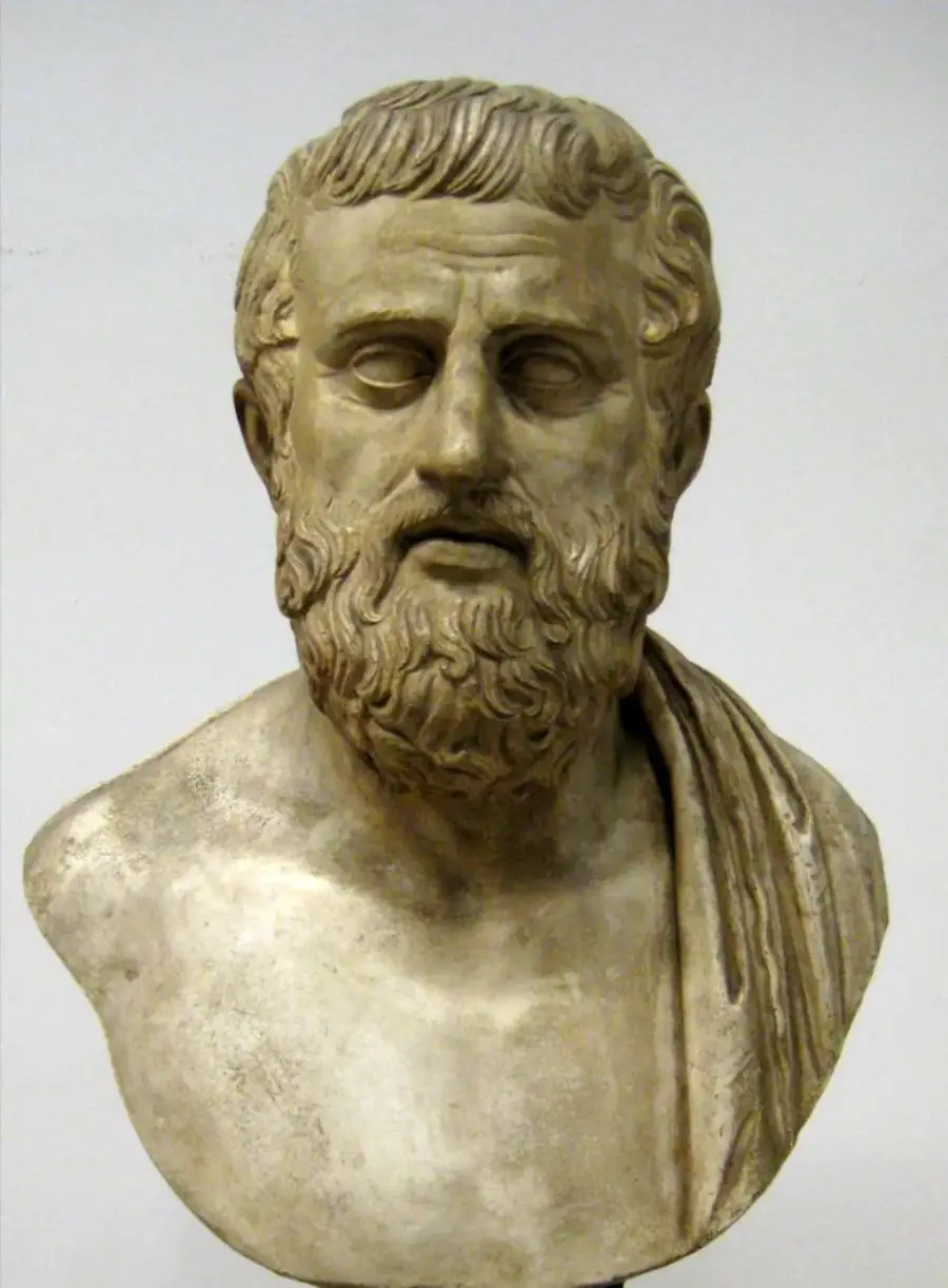 Marble bust of a bearded man with curly hair, draped in a toga over one shoulder, set against a plain background.
