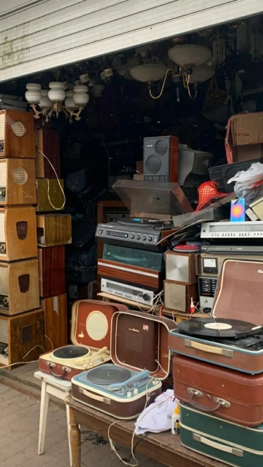 A cluttered shop filled with vintage radios, record players, speakers, and audio equipment stacked closely together, creating a nostalgic and busy atmosphere.