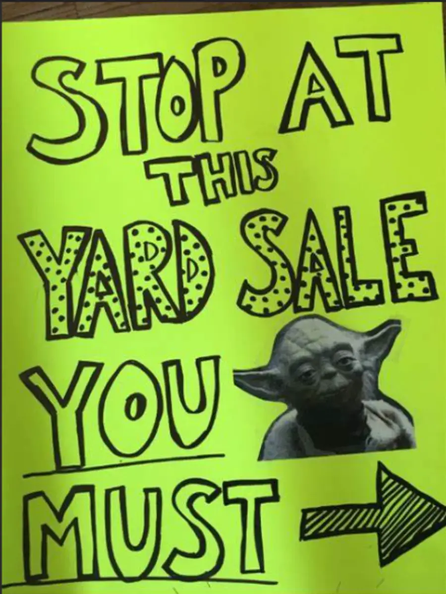 Bright yellow sign with bold black text: “Stop at this yard sale you must,” featuring an image of Yoda’s face and a large right-pointing arrow at the bottom.