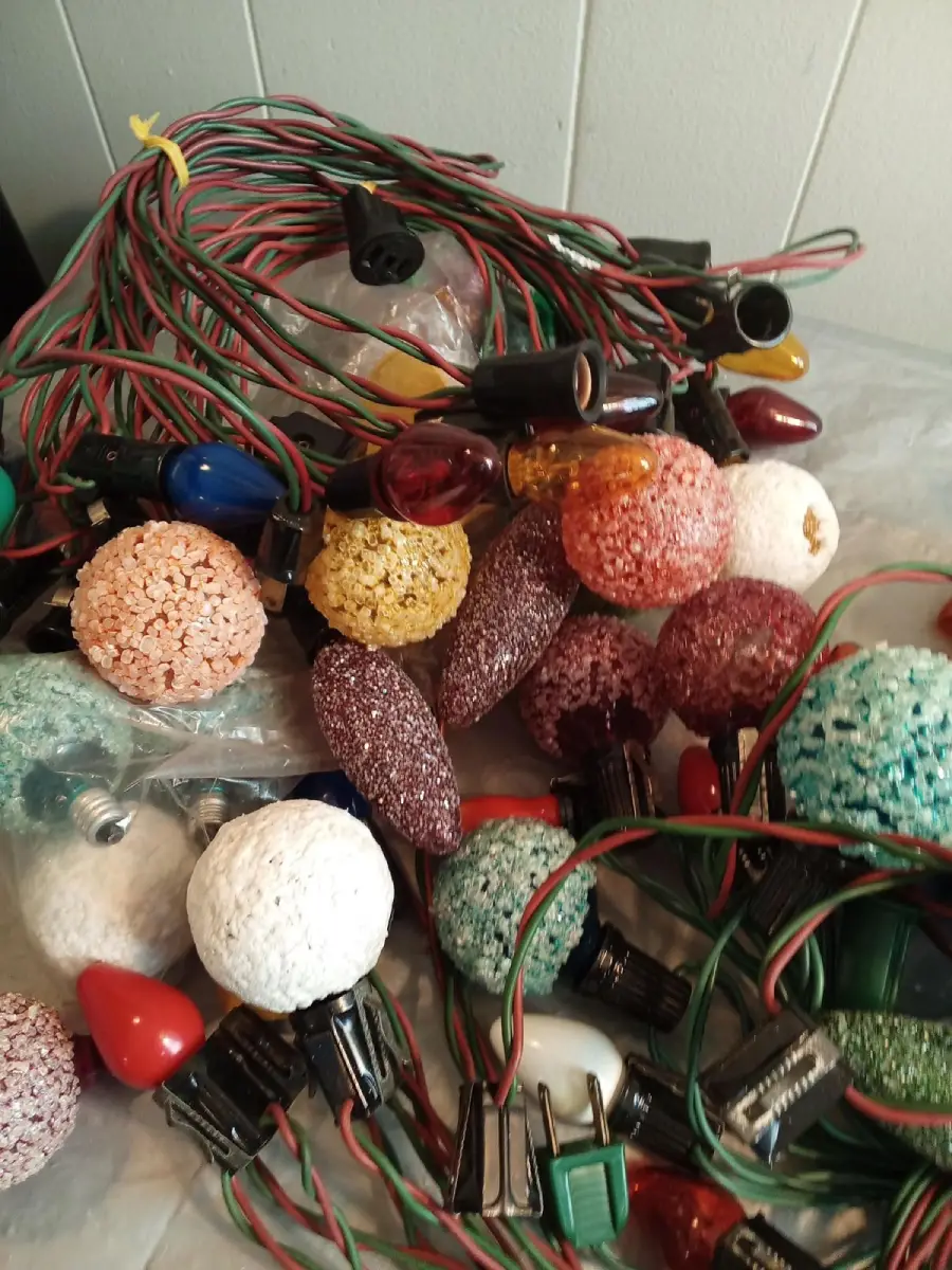 A pile of vintage Christmas lights with colorful textured bulbs and cords, some round and some elongated, spread out on a surface.