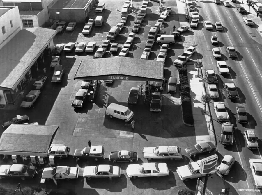 Aerial view of long lines of cars at a gas station, with vehicles filling the street and parking lot, likely during a fuel shortage.