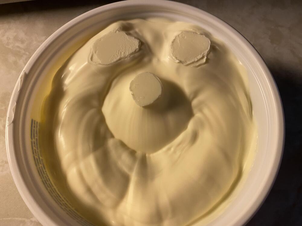 A tub of margarine with three scoops taken out, forming the shape of a smiling face with two eyes and a round nose.