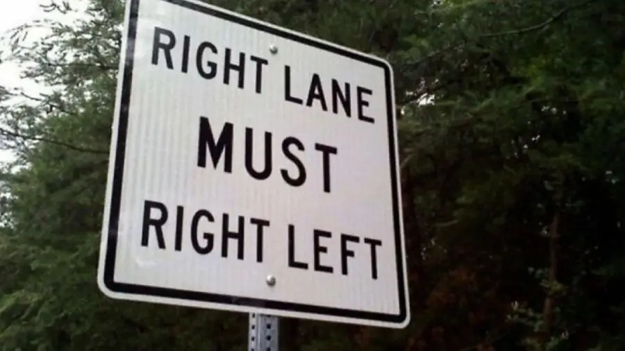 A street sign reads “RIGHT LANE MUST RIGHT LEFT” with trees in the background. The sign appears confusing or incorrect due to its contradictory wording.
