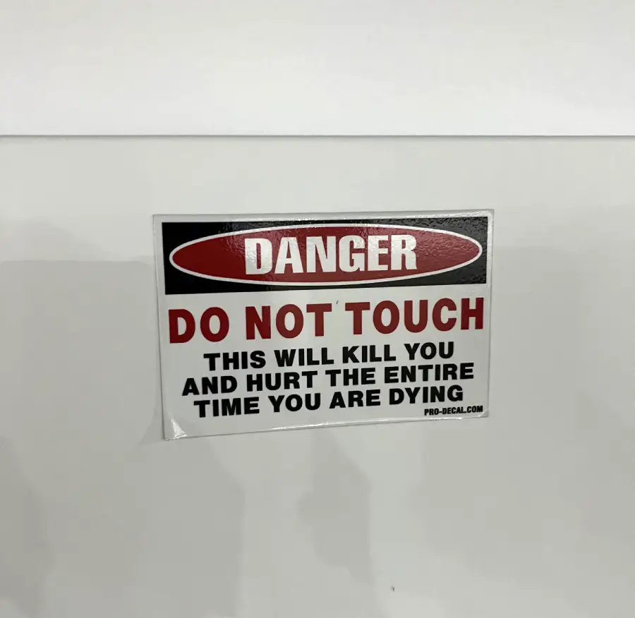 A warning sign reads: “Danger. Do not touch. This will kill you and hurt the entire time you are dying.” The sign has black and red text on a white background.