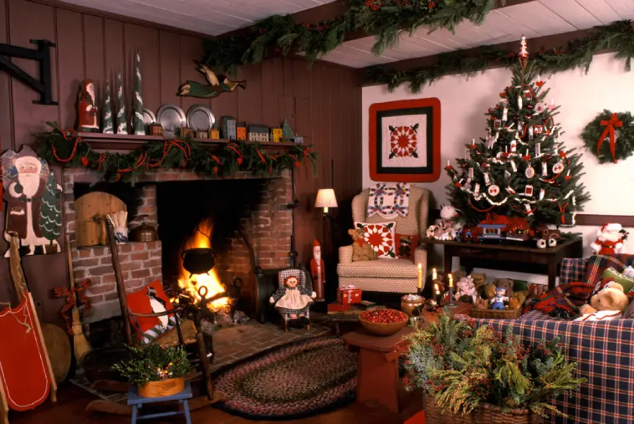 A cozy living room decorated for Christmas with a lit fireplace, a decorated tree, wreaths, garland, stockings, wrapped gifts, and holiday-themed figurines throughout the room.