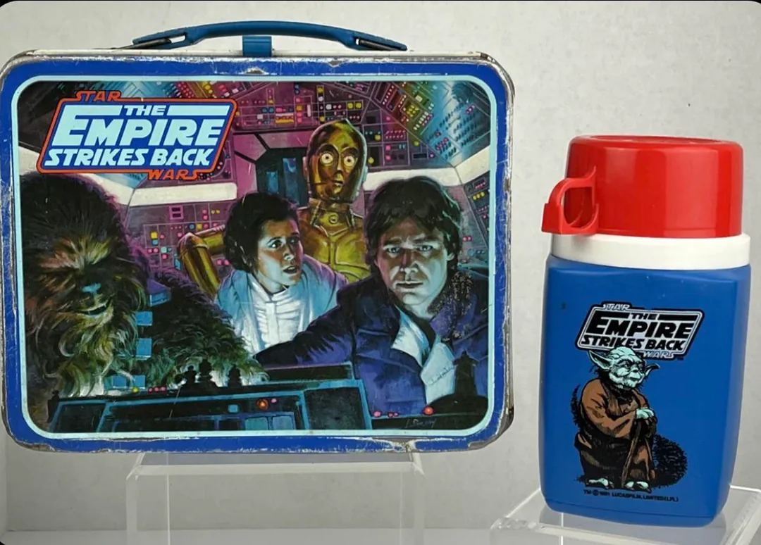 A Star Wars: The Empire Strikes Back lunchbox featuring Chewbacca, Princess Leia, C-3PO, and Han Solo, with a matching blue thermos displaying an illustration of Yoda.