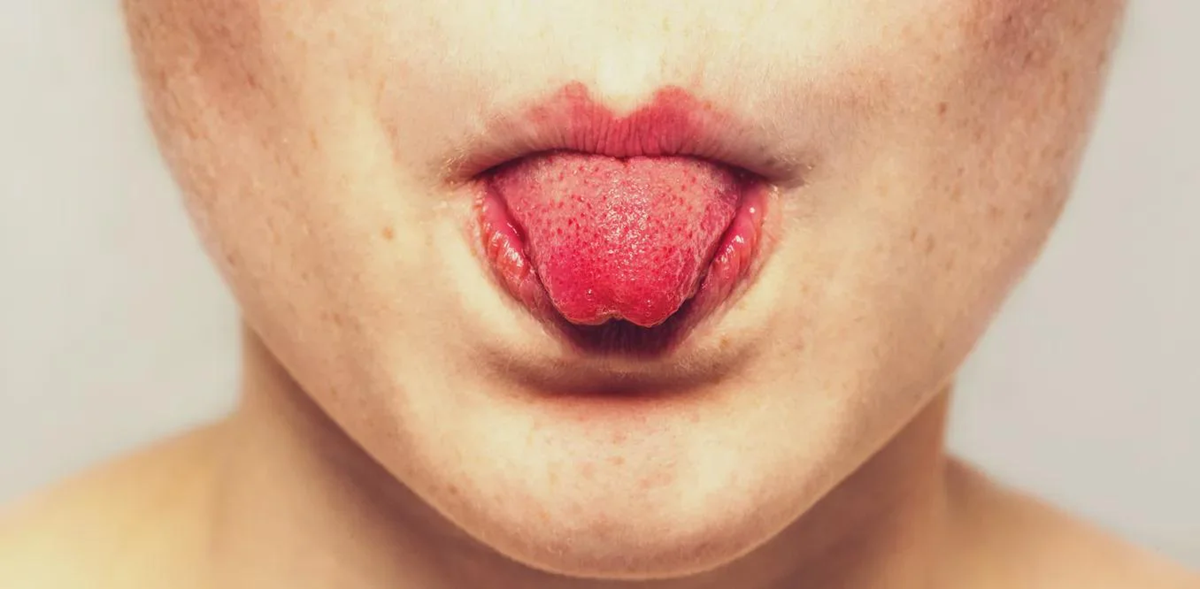 A close-up of a person sticking out their tongue, which is curled upwards. The lower half of the face, lips, and chin are visible.
