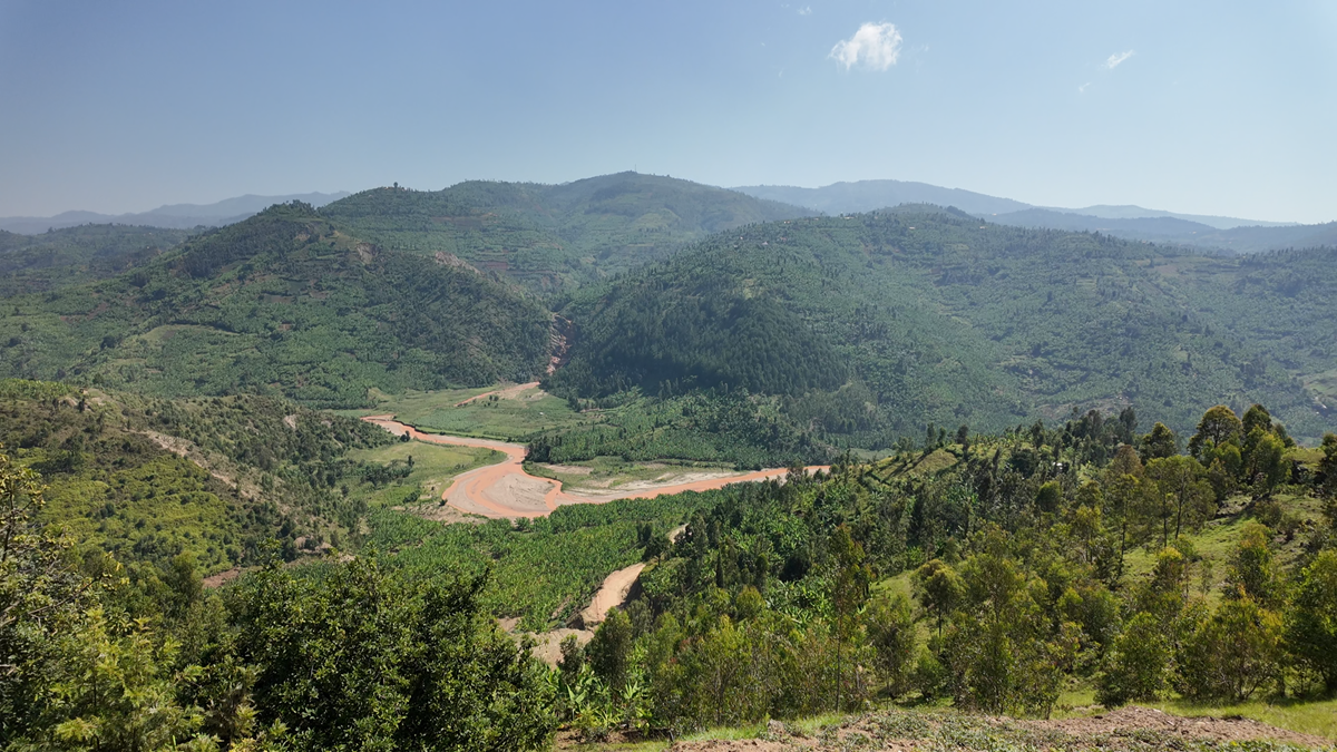 A lush green landscape with rolling hills, a winding river, and a clear blue sky with one small cloud. Dense vegetation covers the hills and valley.