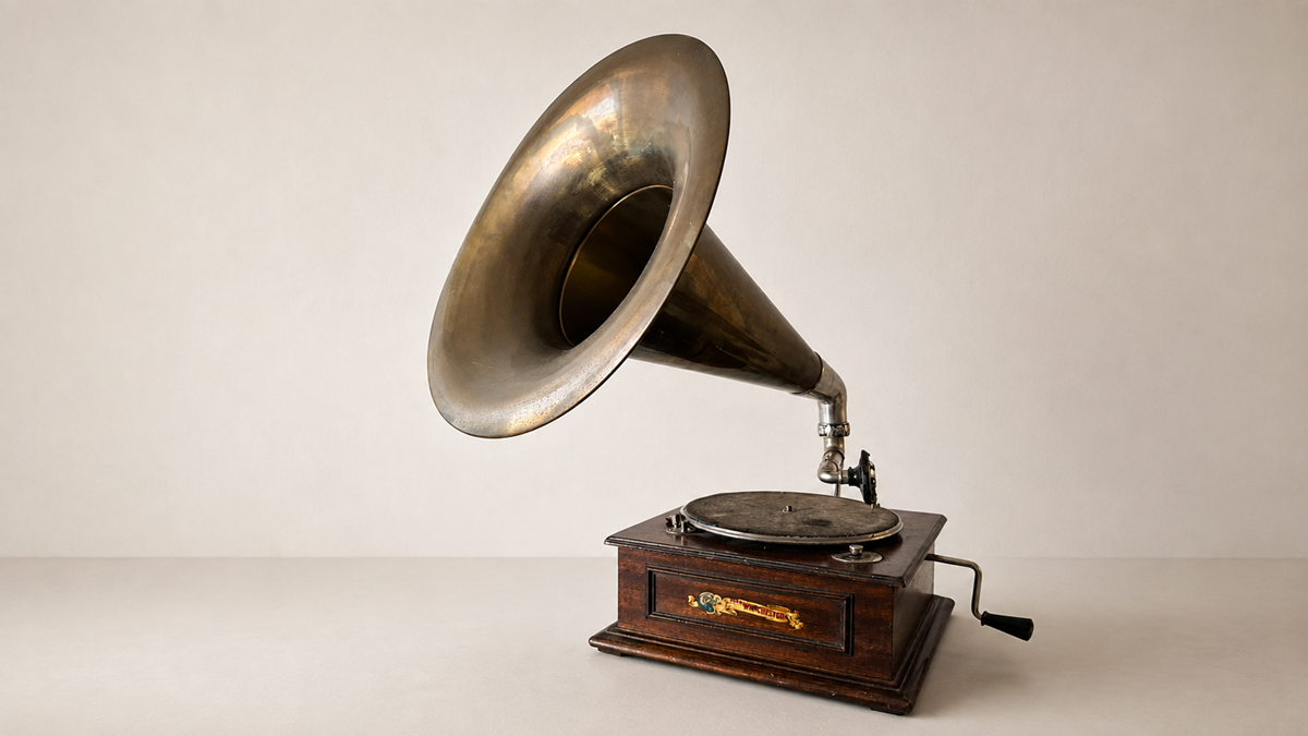 A vintage gramophone with a large brass horn, wooden base, and crank handle, set against a plain light-colored background.