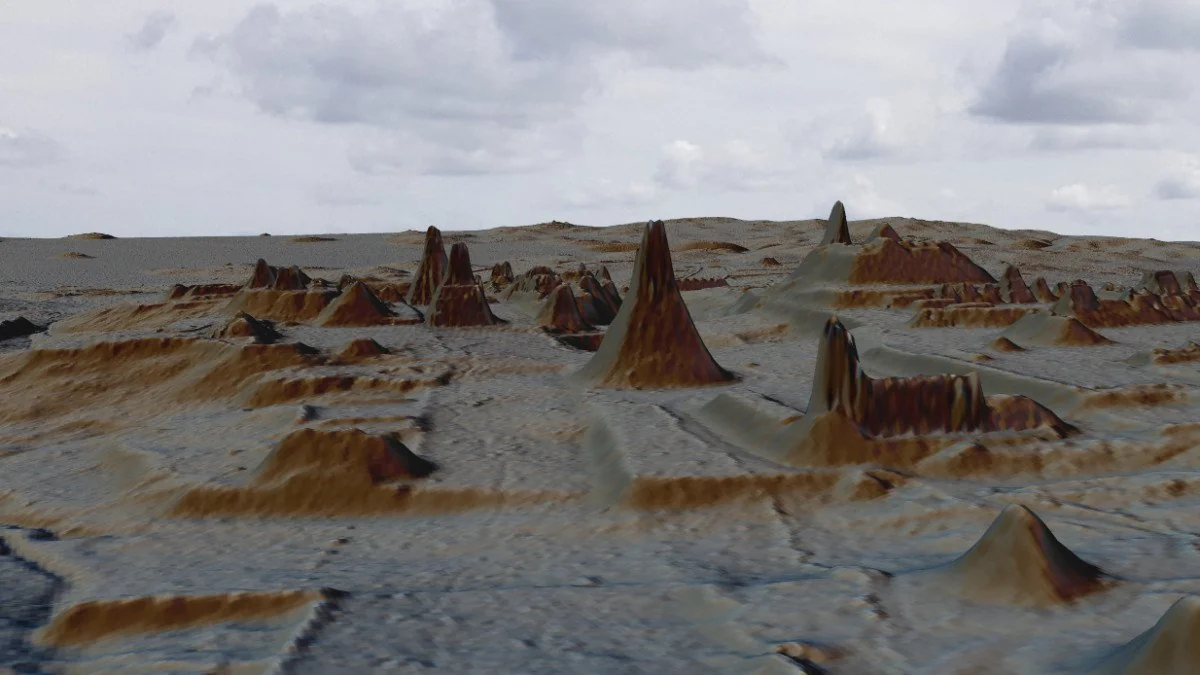 A computer-generated landscape with rough, mountainous terrain and jagged peaks under a cloudy sky. The ground appears textured and uneven, with several tall, sharp formations scattered throughout.