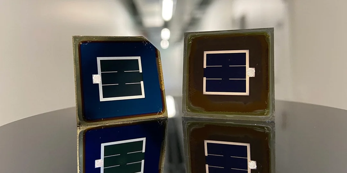 Two small square solar cells with grid patterns stand on a reflective surface in a brightly lit hallway, showing clear reflections of their shapes and designs.