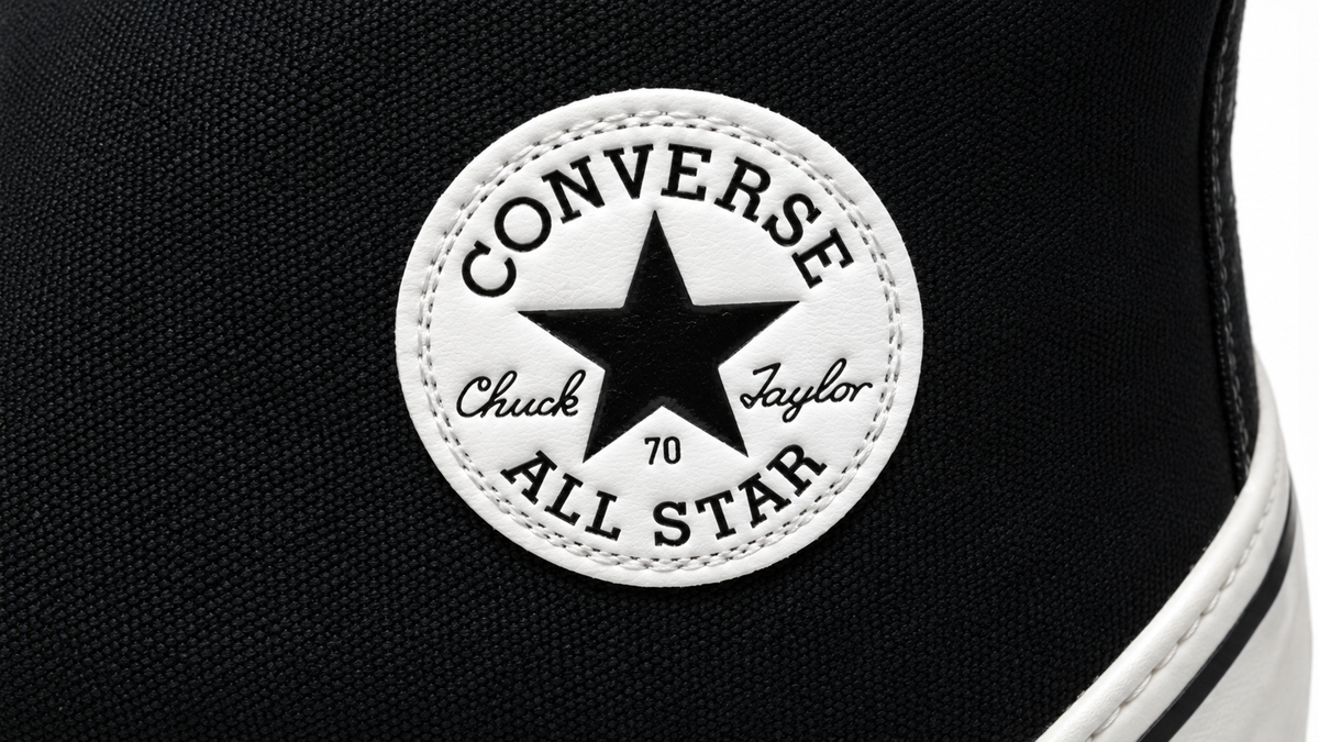 Close-up of a black Converse Chuck Taylor All Star shoe, showing the white circular logo patch with a black star and the words “Converse All Star Chuck Taylor 70.”