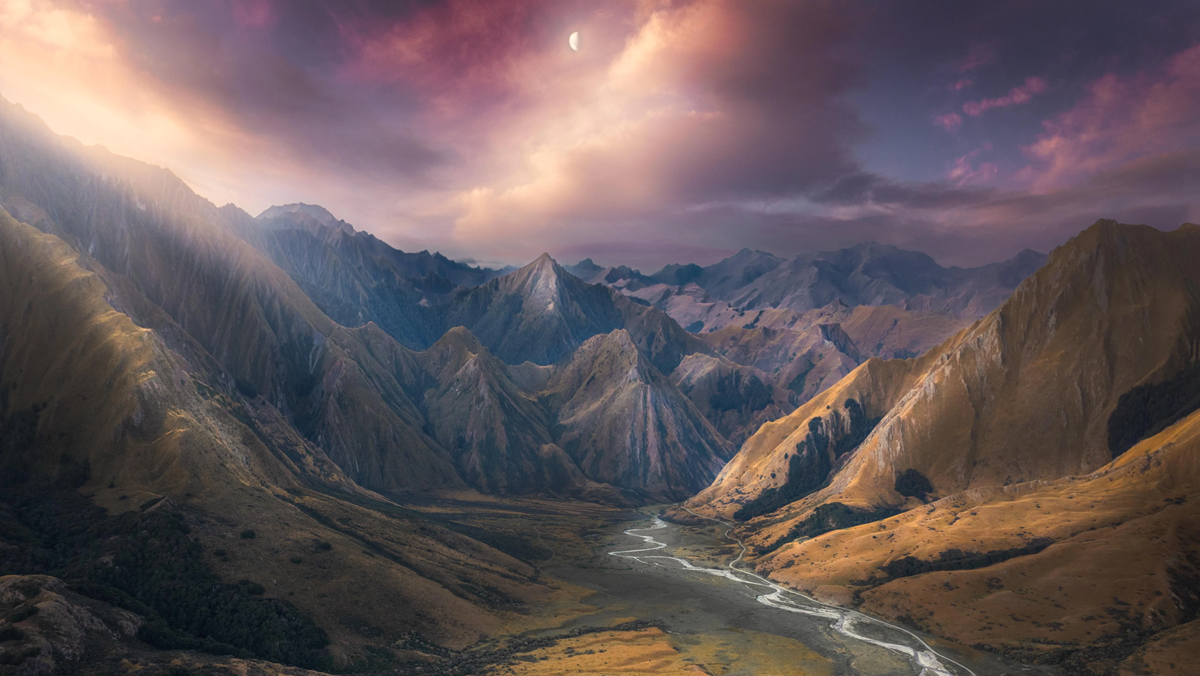 A winding river flows through a wide valley surrounded by rugged, sunlit mountains under a colorful sky with clouds and a crescent moon.