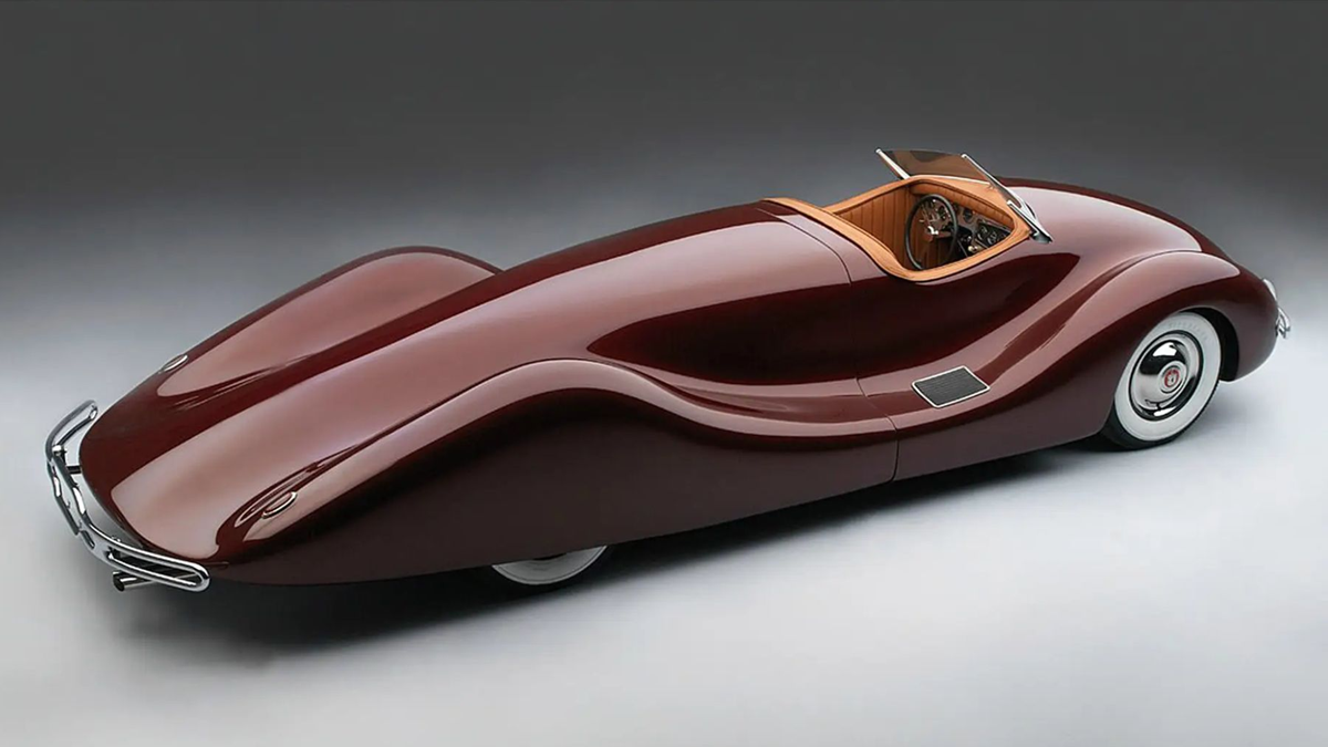 A sleek, vintage-style maroon car with smooth, flowing curves, a small windshield, and a tan interior, viewed from above on a gray background.