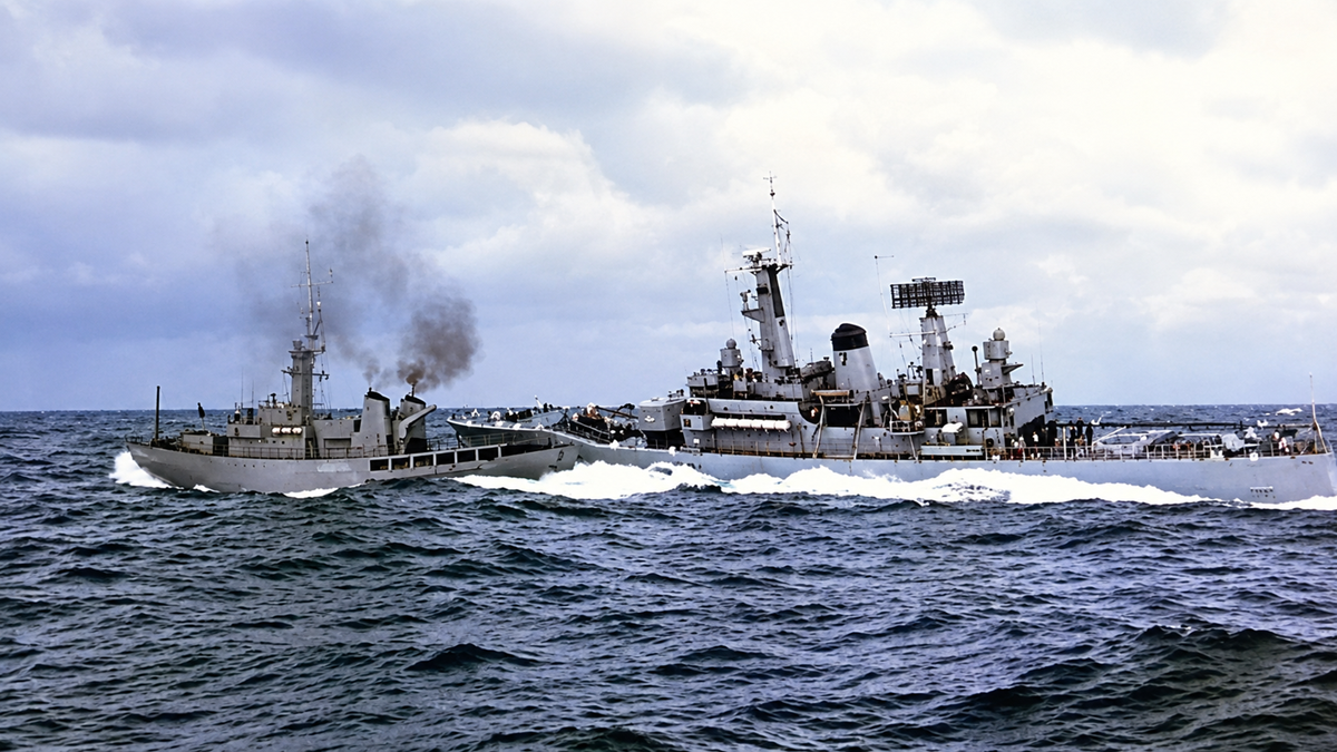 Two navy ships collide at sea, with one ship visibly damaged and emitting smoke. The ocean is choppy, and the sky is cloudy, creating a dramatic scene of the maritime accident.