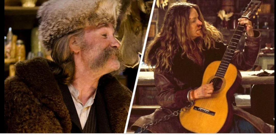 Two people in fur coats indoors; one wears a fur hat and has large sideburns, while the other, with long hair, sits holding a guitar and is chained by the ankle.