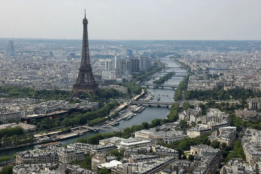 Aerial view of Paris with the Eiffel Tower, the Seine River, and surrounding buildings under a slightly cloudy sky.