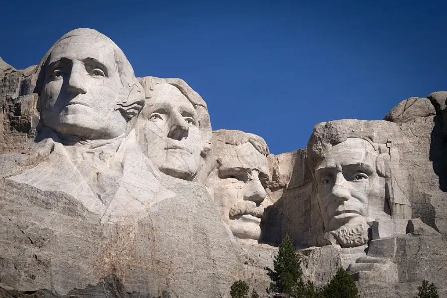 Mount Rushmore National Memorial with four large carved faces of U.S. presidents on a granite mountainside against a clear blue sky.