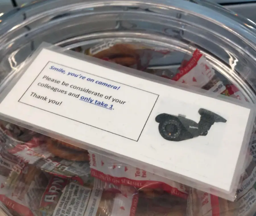 A container of individually wrapped snacks has a sign with a camera image, reminding people to smile, be considerate, and only take one snack.