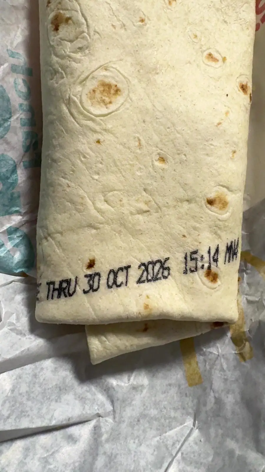 A wrapped burrito with a printed expiration date and time: “THRU 30 OCT 2026 15:14 MA” on the tortilla.