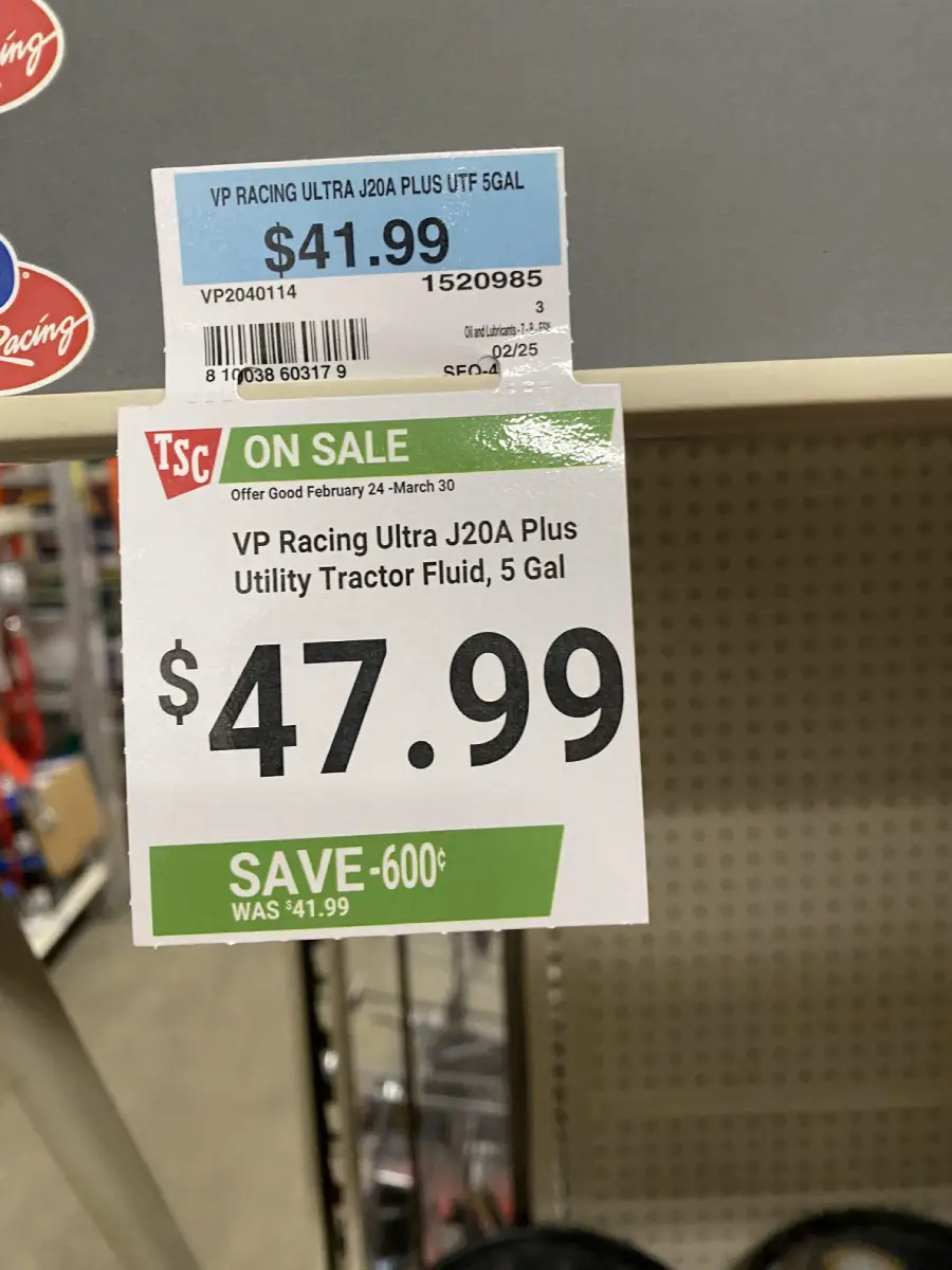 Two price tags for VP Racing Ultra J20A Plus Utility Tractor Fluid, 5 gal: one shows $41.99, the other shows $47.99 with a sale notice and a “save 60¢” label. Both tags hang from a store shelf.