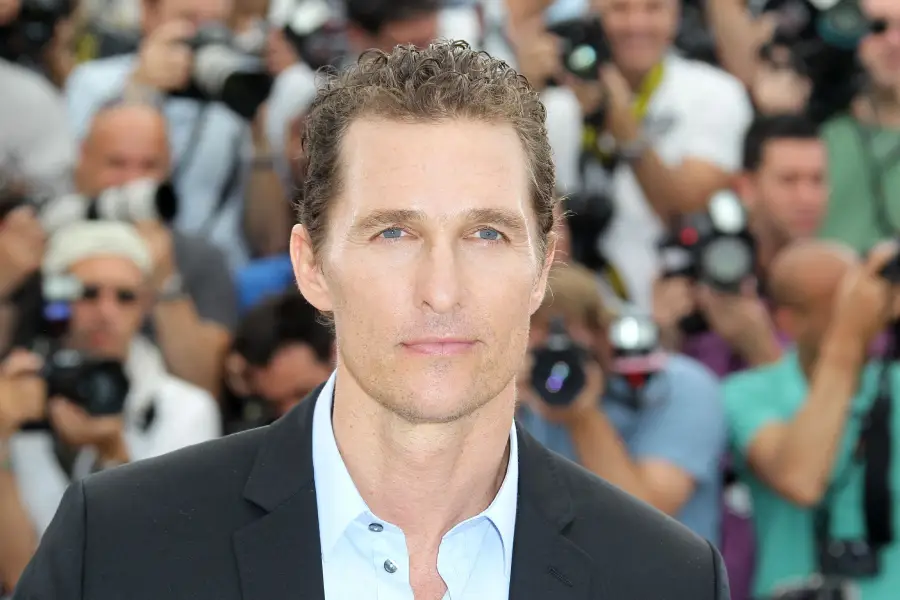 A man in a suit poses for photos on a red carpet, surrounded by photographers and cameras in the background.