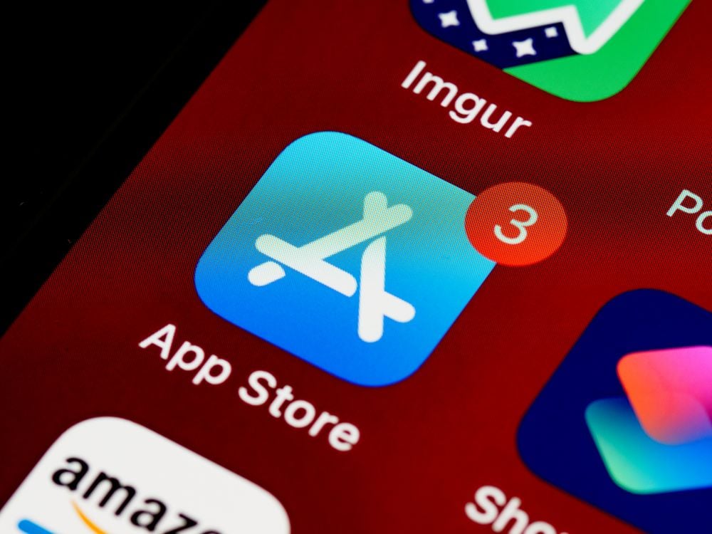 Close-up of the App Store icon on a phone screen with a red notification badge showing the number three. Other app icons are partially visible in the background.