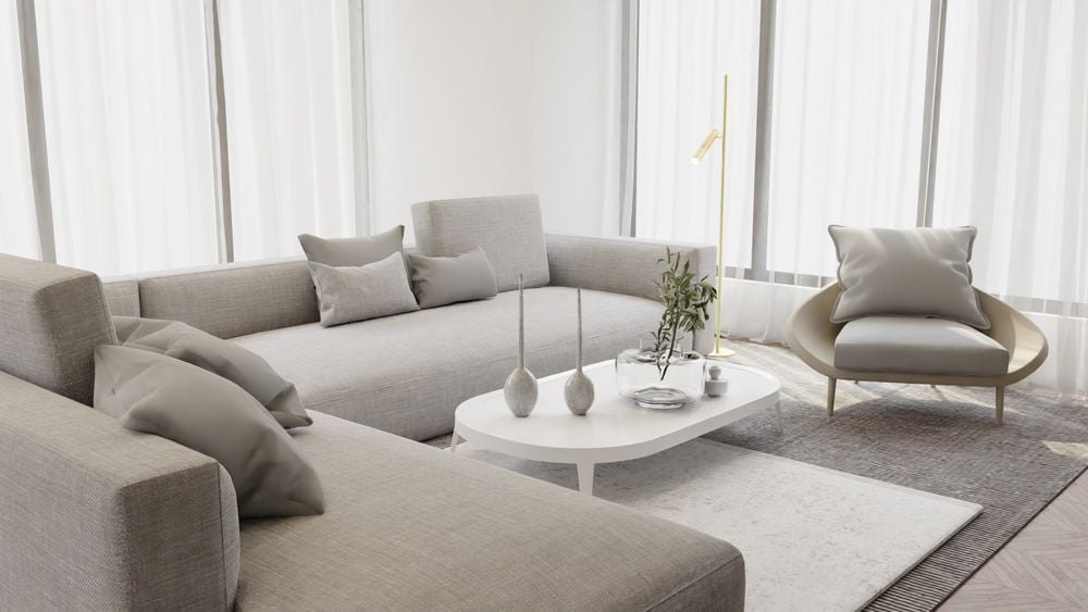 Modern living room with light gray sofas, a matching armchair, and a white coffee table with candles and a plant. Large windows with sheer curtains let in natural light.