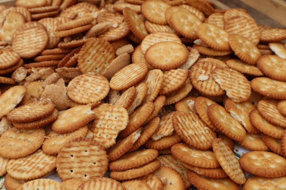 A large pile of round, golden brown crackers, some plain and some with a textured surface. A few are broken, and the crackers are stacked and scattered closely together.