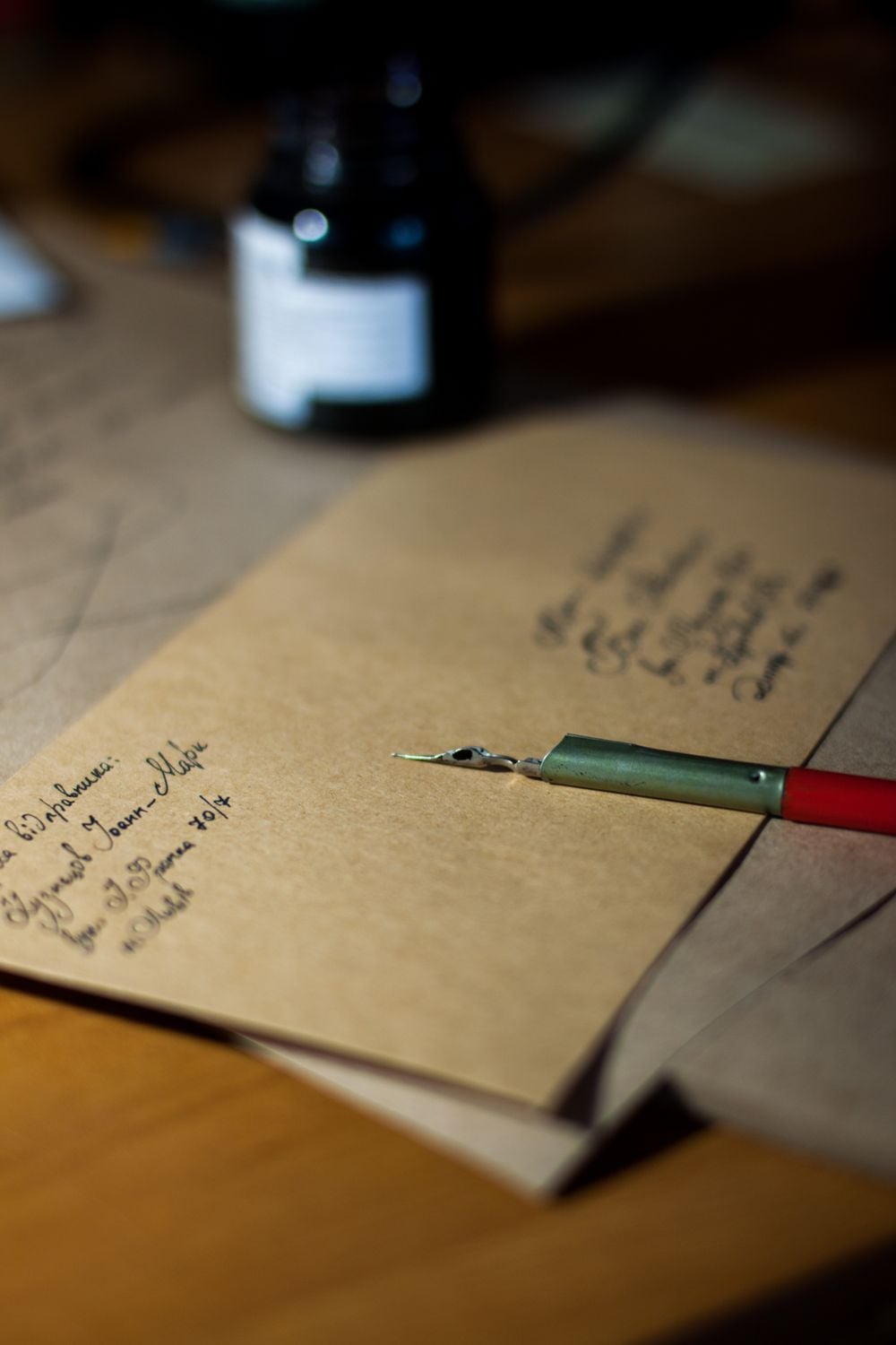 A handwritten letter on brown paper sits on a desk with a dip pen and an ink bottle nearby, suggesting someone is in the process of writing a letter.