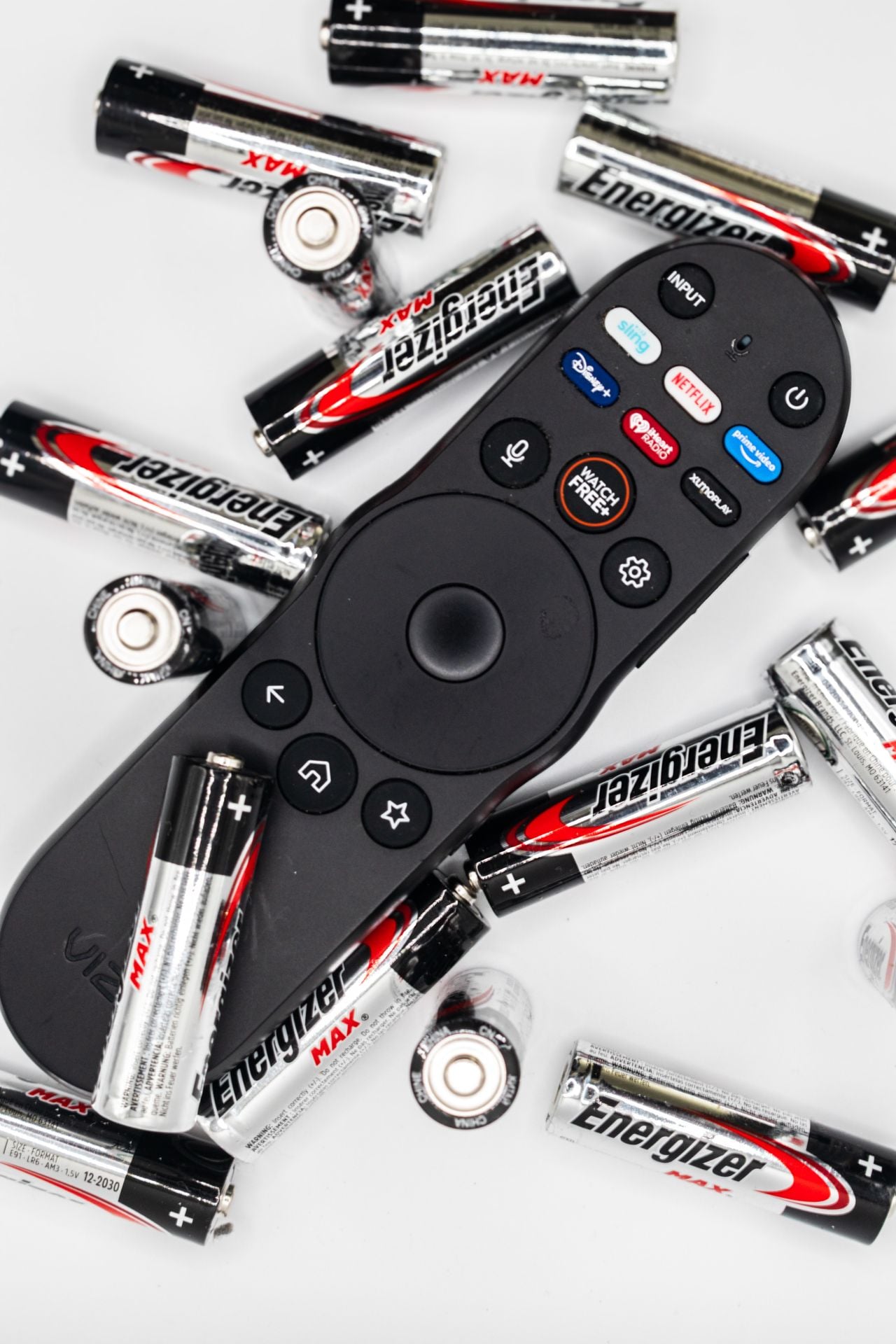 A black TV remote control surrounded by several Energizer AA and AAA batteries, some standing and some lying down, on a white surface.
