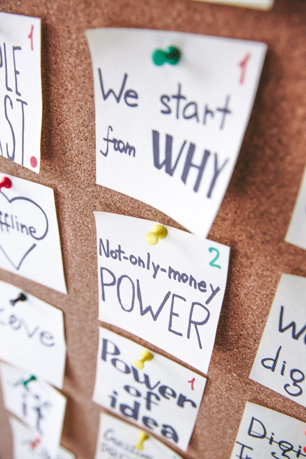 Sticky notes pinned to a corkboard, featuring handwritten phrases like “We start from WHY” and “Not-only-money POWER,” each labeled with numbers in red or green ink.