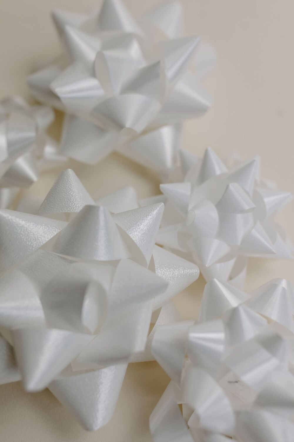 Several shiny, white gift bows of various sizes are arranged on a light beige surface, creating a festive and decorative appearance.
