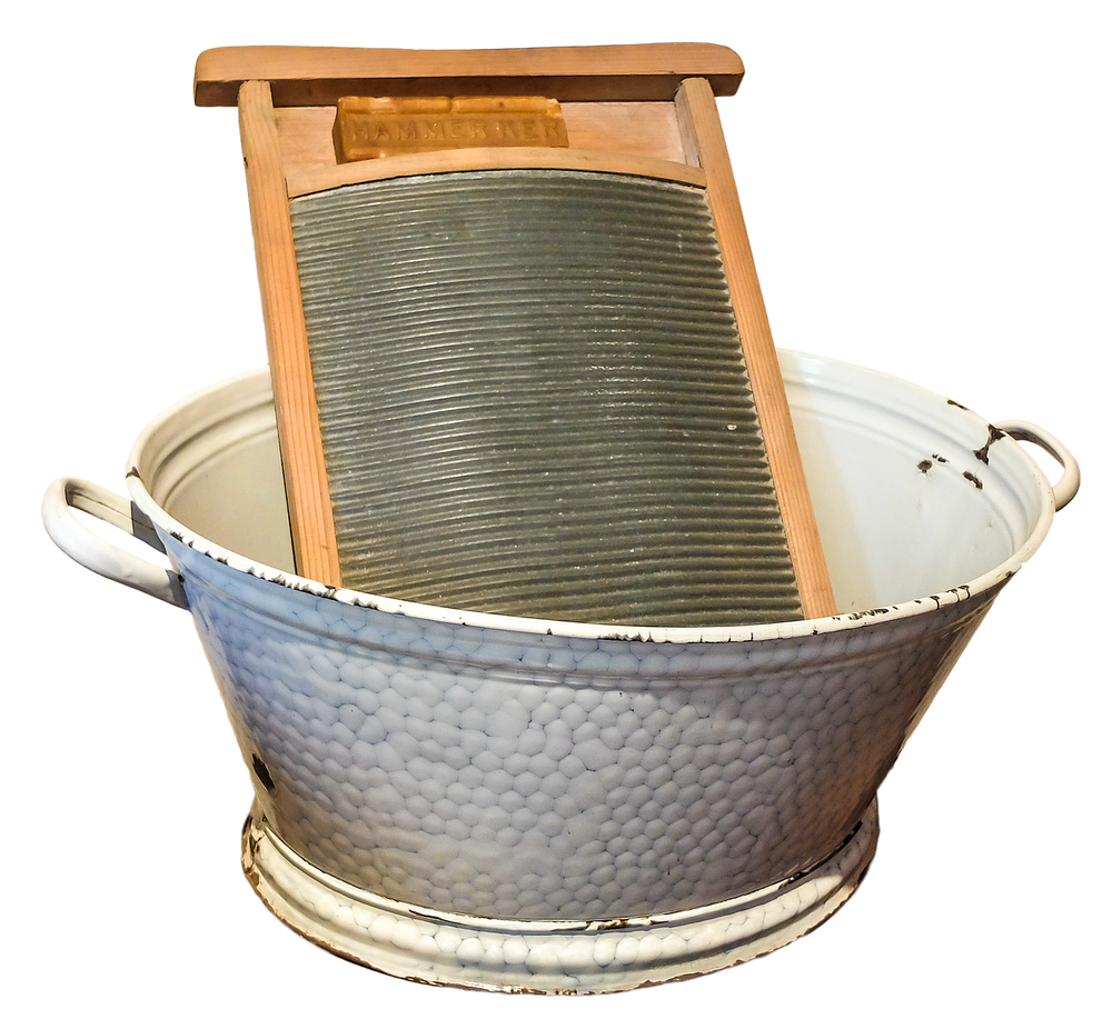 A vintage metal washboard rests inside a large white enamel washbasin with handles, both items showing signs of age and use.
