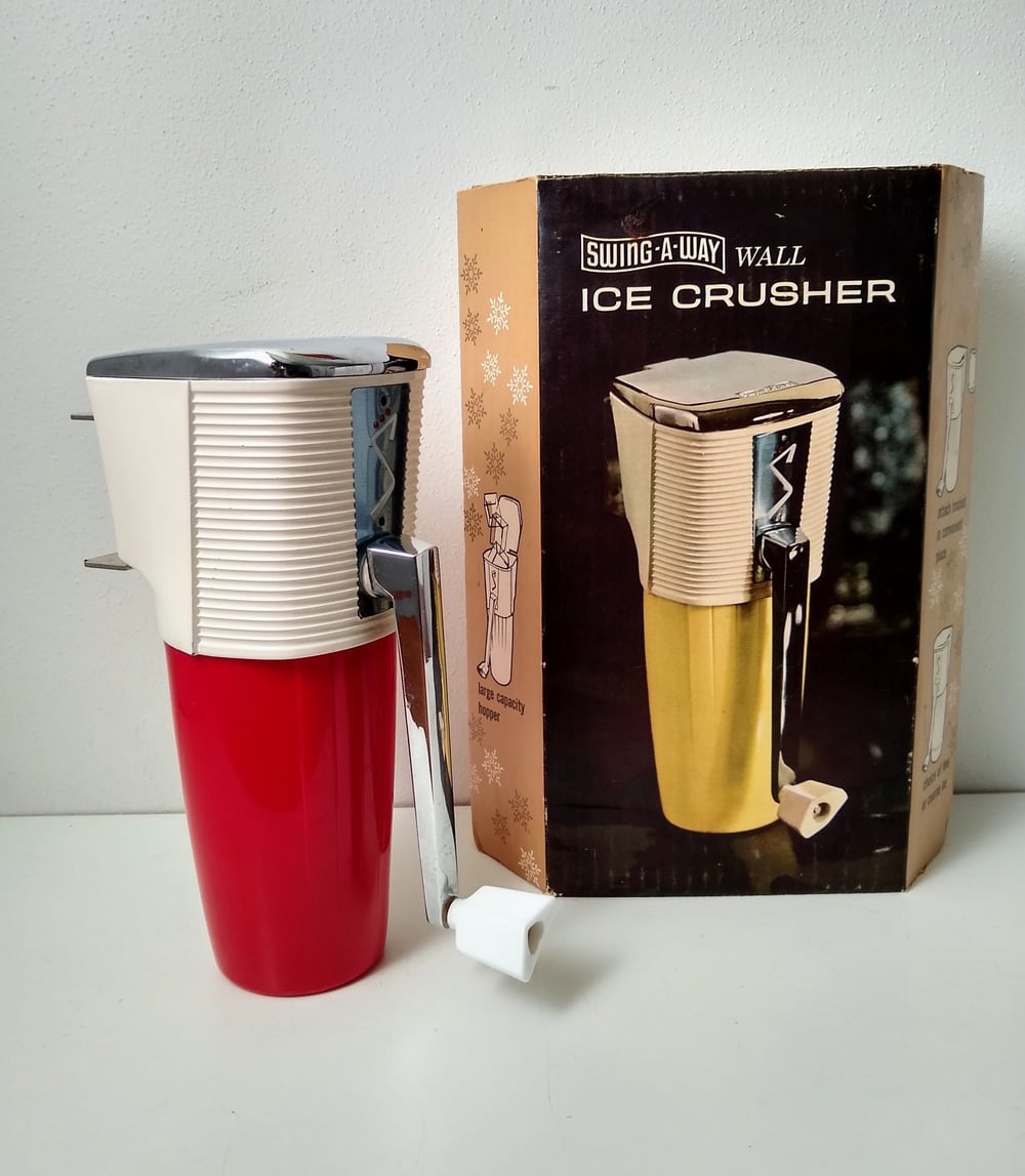 A red and white manual wall ice crusher with a crank handle sits next to its original box, which shows an image of the product and the label “Swing-A-Way Wall Ice Crusher.”