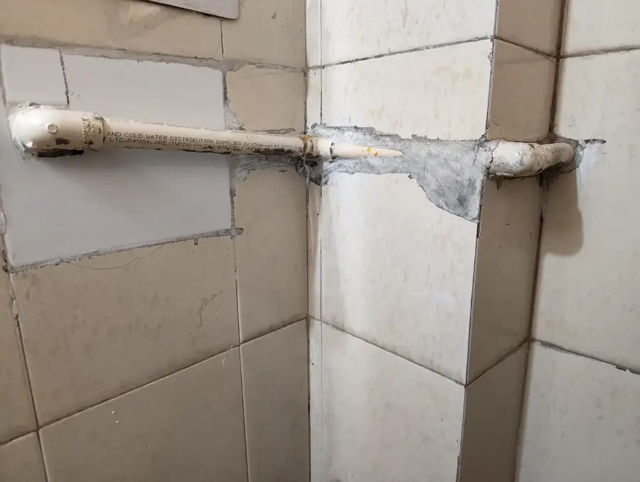 A white pipe runs through tiled walls at a corner, with rough cement patches around it, indicating a recent or makeshift installation or repair.