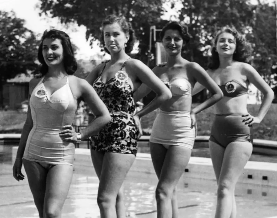 Four women in vintage swimsuits stand side by side by a pool, posing with hands on hips and smiling. Trees and outdoor scenery are visible in the background.