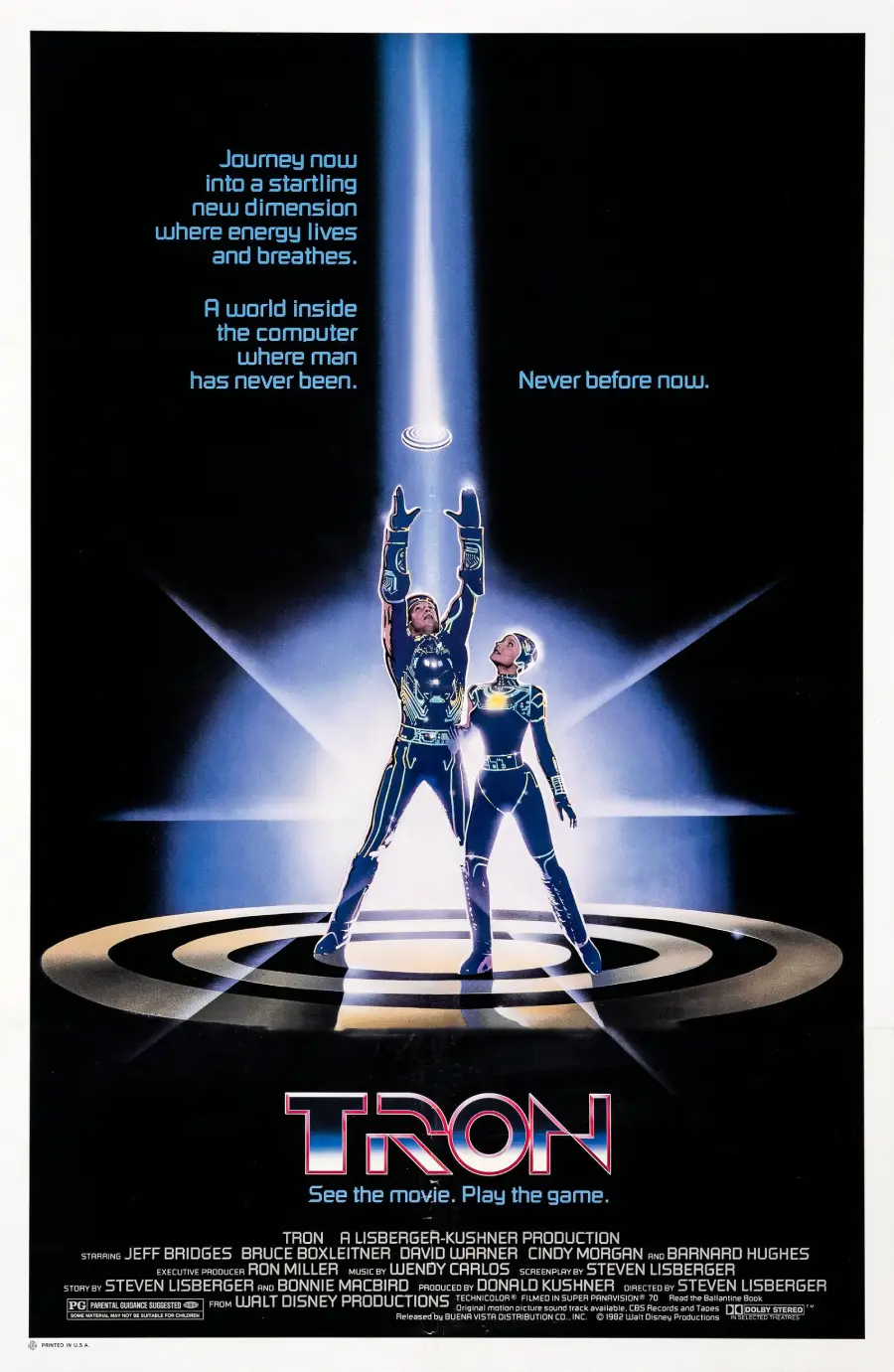 Two figures in futuristic suits stand on a glowing platform, one lifting a disc overhead with light streaming up. The poster text reads “TRON. See the movie. Play the game.” with additional film credits.