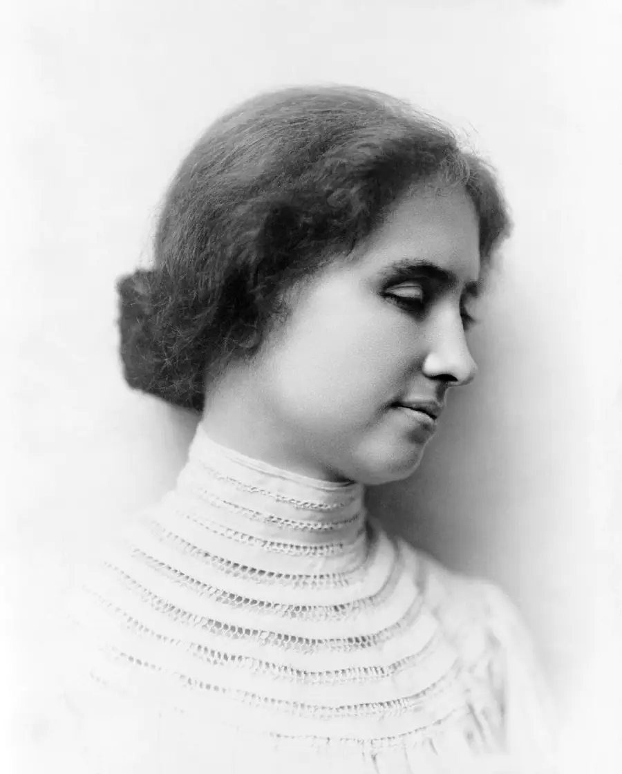 A young woman with her hair in a bun, wearing a high-necked, textured white blouse, is shown in profile against a light background.