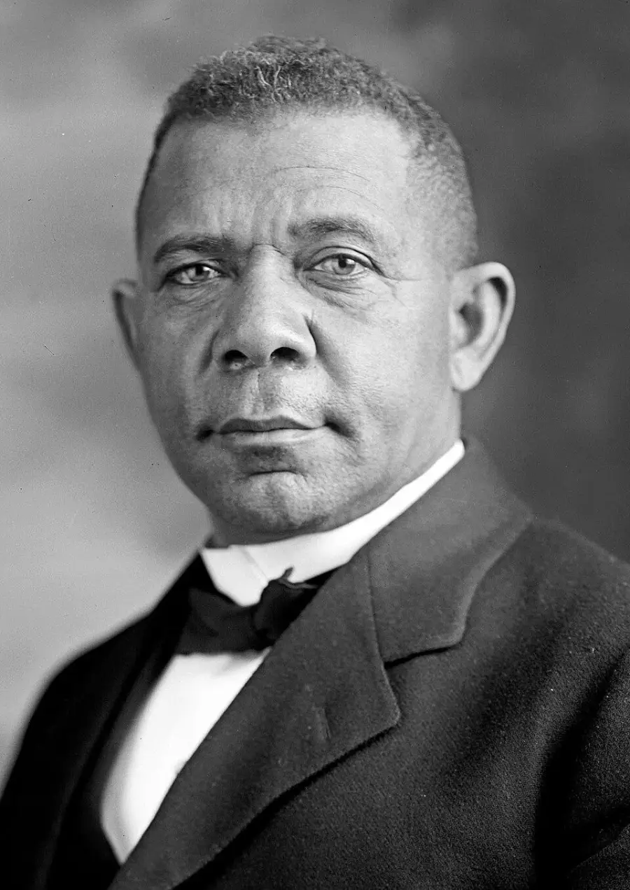 A Black man in formal attire with a bow tie and jacket looks directly at the camera against a plain background.