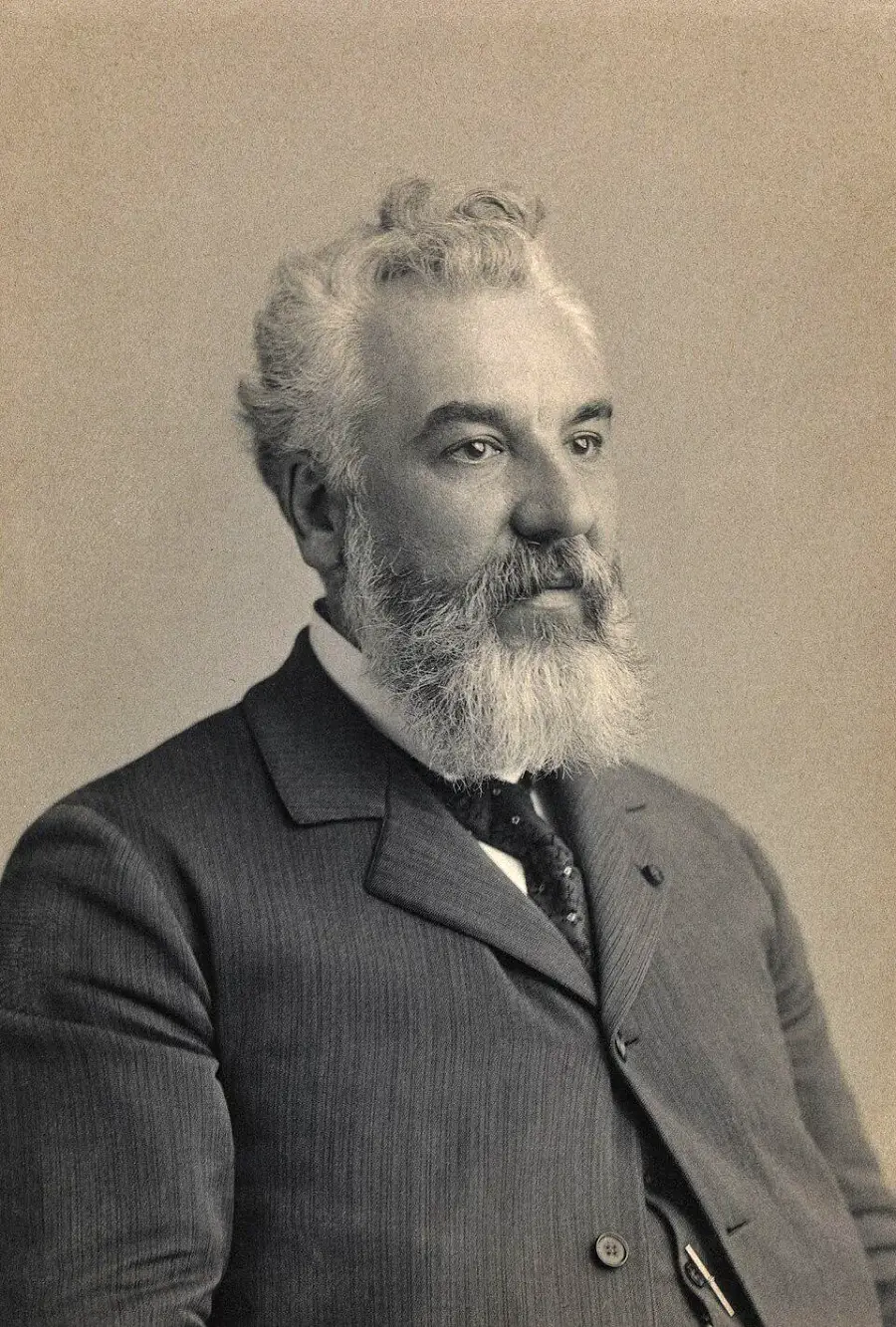 Black and white portrait of an older man with white hair and a full beard, wearing a striped suit and tie, looking slightly to the side against a plain background.