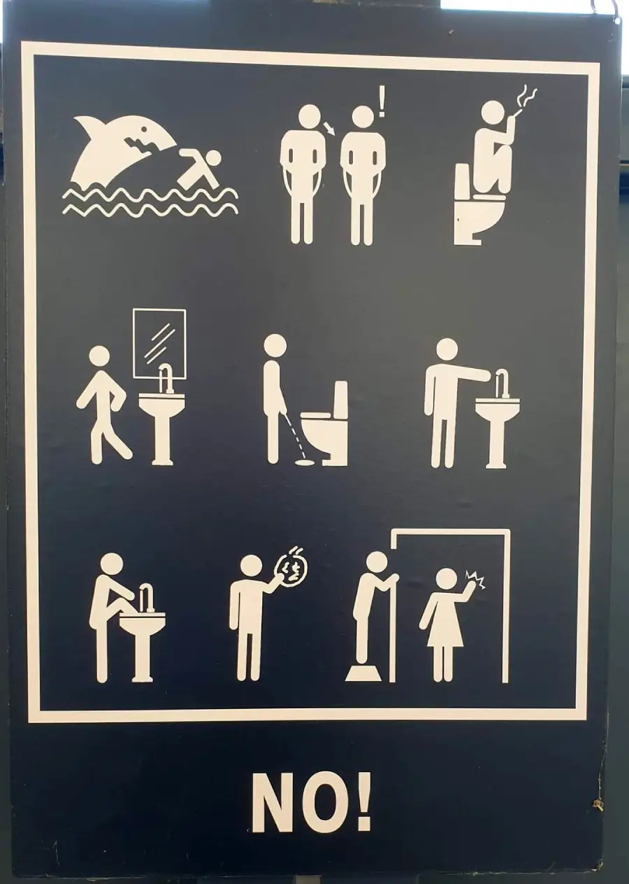 Sign with illustrations showing what NOT to do in a bathroom: swimming, crowding, smoking, undressing, urinating outside toilets, eating, vandalizing, vomiting, and hanging; bold “NO!” at the bottom.