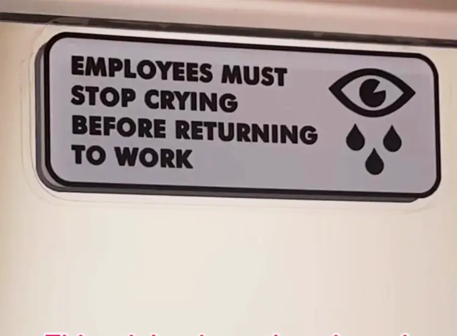 A sign reads “Employees must stop crying before returning to work” with an eye icon shedding three teardrops.