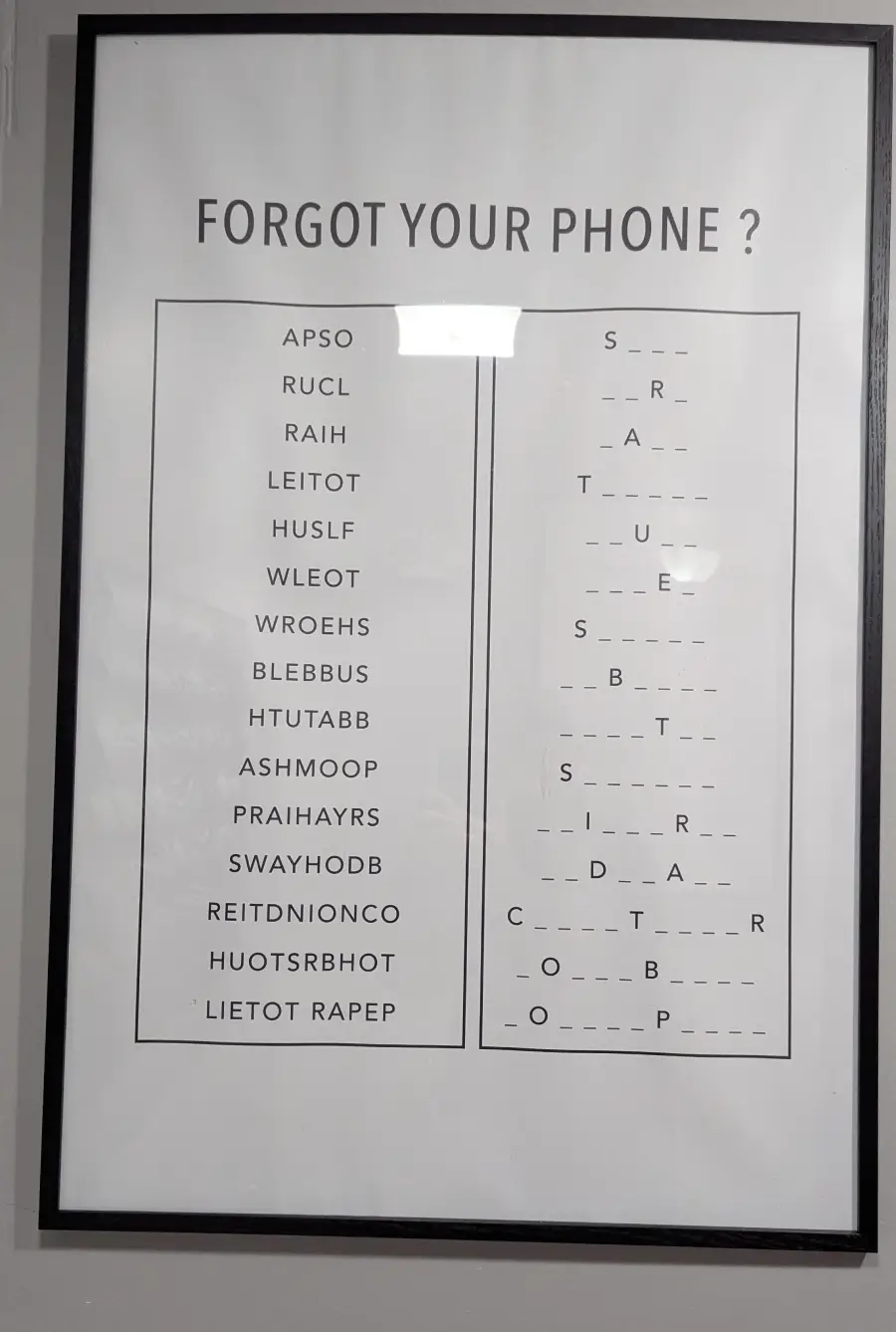 A framed sign asks “Forgot your phone?” and shows two columns: one with scrambled words, another with hangman-style blanks to fill in as word puzzles. The background is white with black text.