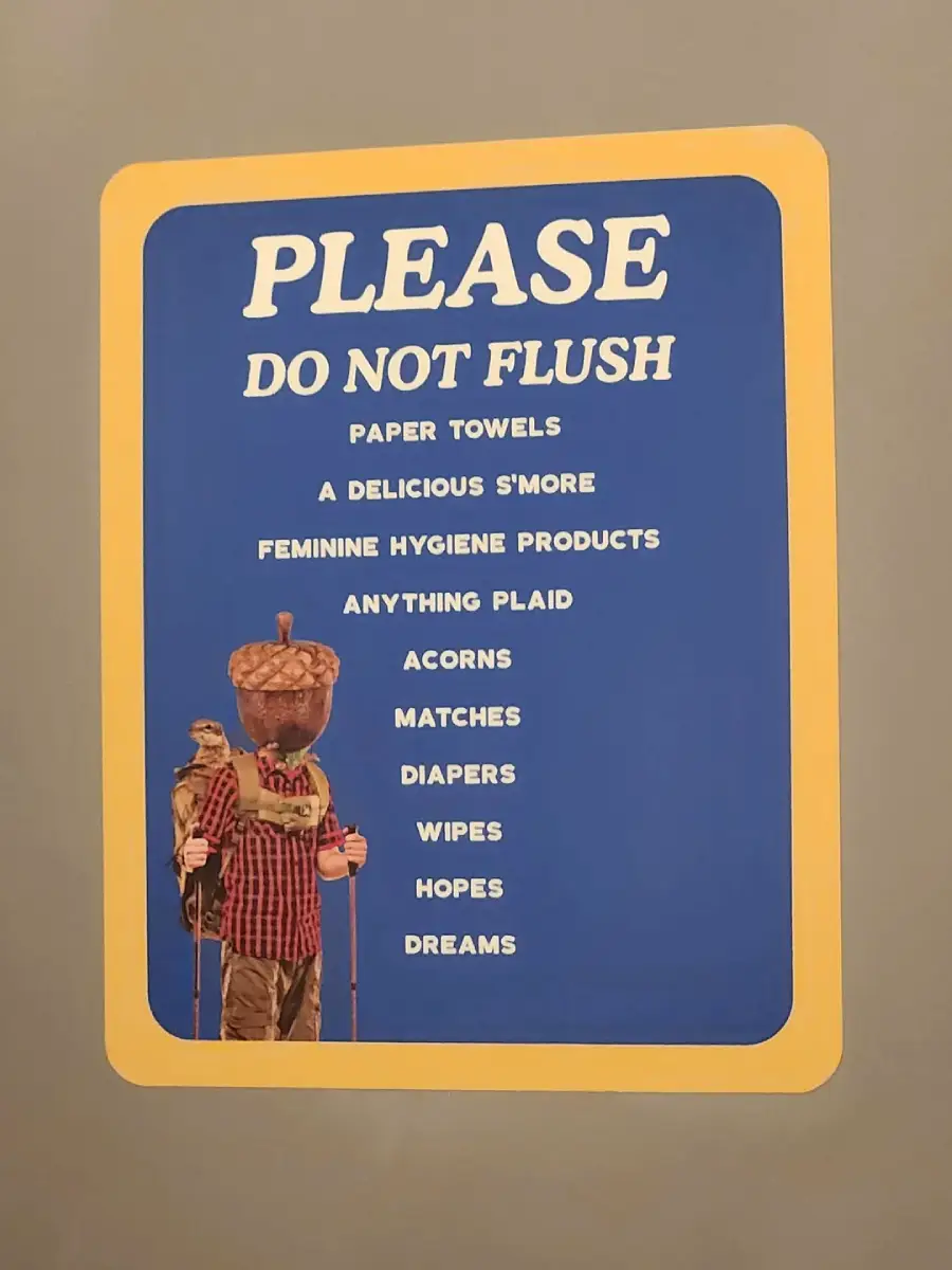 A humorous sign reading “PLEASE DO NOT FLUSH” lists items like paper towels, s’more, feminine products, anything plaid, acorns, matches, diapers, wipes, hopes, and dreams, with a hiker whose head is an acorn at the bottom.