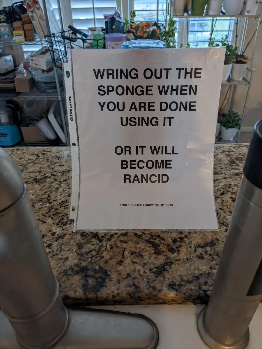 A sign on a kitchen counter reads: “Wring out the sponge when you are done using it or it will become rancid. (You should all know this by now).”
