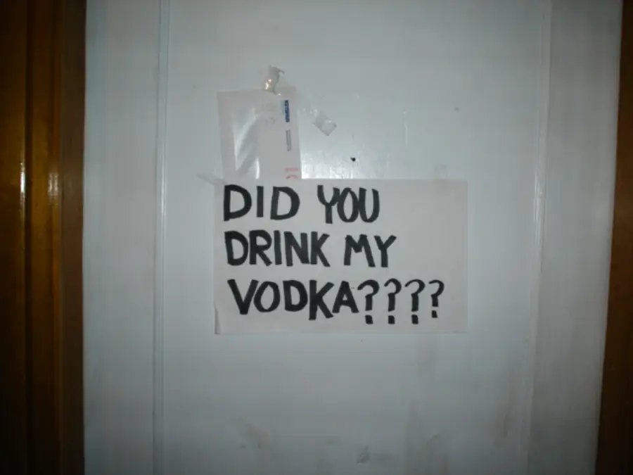 A handwritten sign on a door reads, “DID YOU DRINK MY VODKA????” with five question marks. There are some papers and tape stuck above the sign.