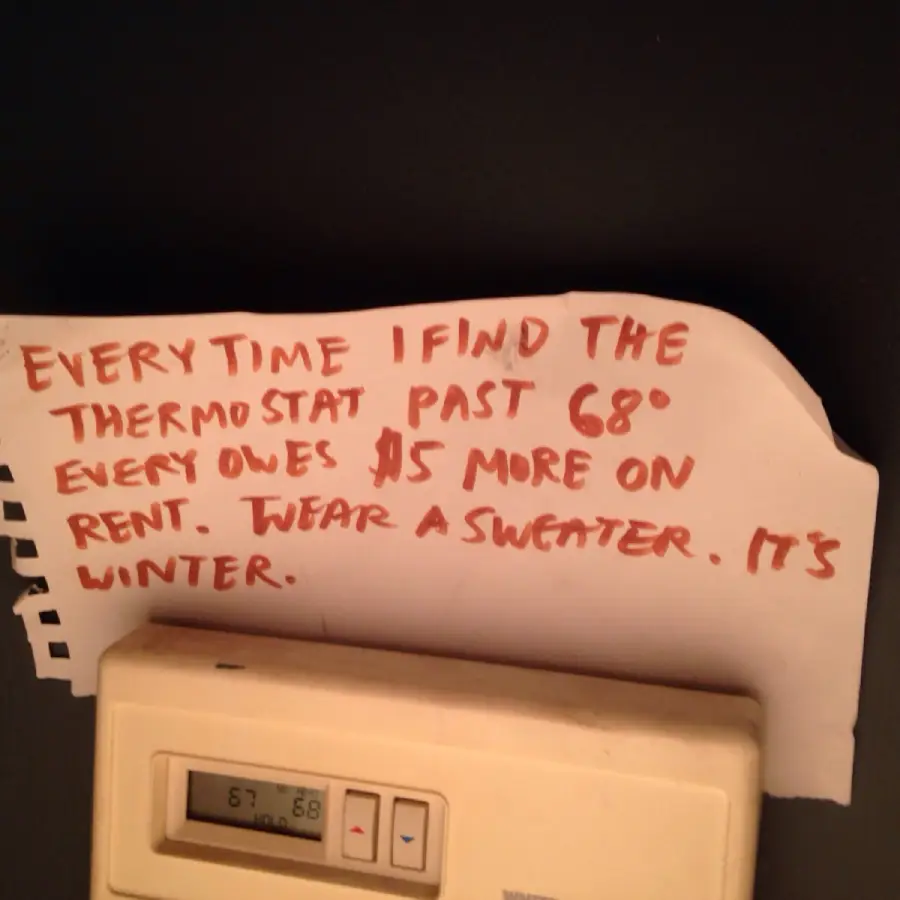 A handwritten note above a thermostat reads: “Every time I find the thermostat past 68°, everyone owes $5 more on rent. Wear a sweater. It’s winter.”