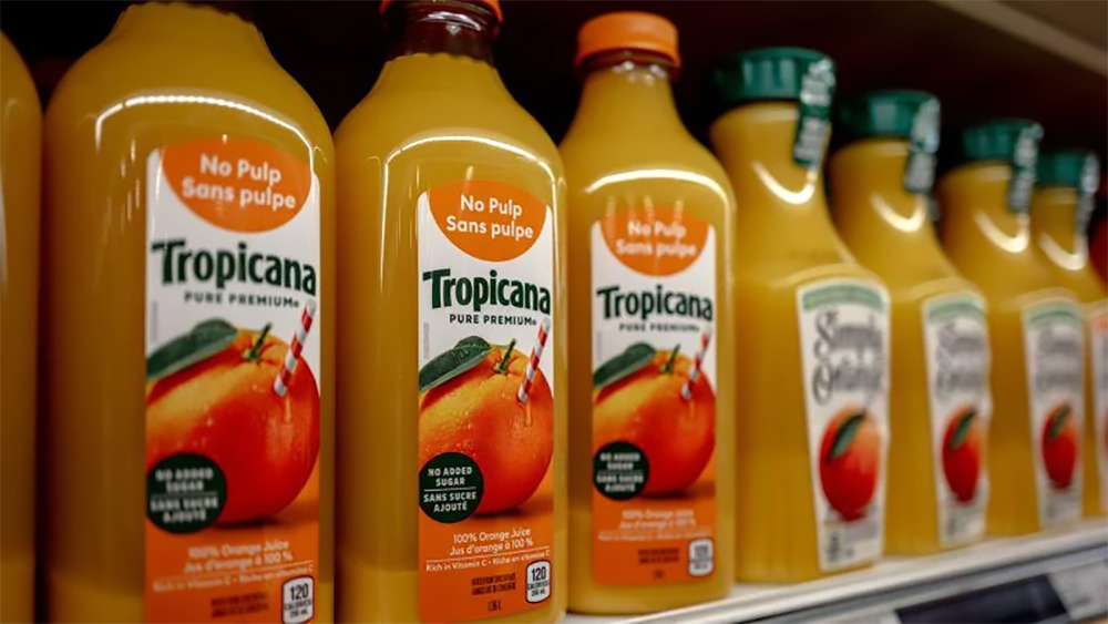 Bottles of Tropicana orange juice labeled “No Pulp” are lined up on a grocery store shelf. The bottles are mostly orange with green caps and colorful labels, and other branded juice bottles are visible next to them.
